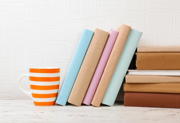 Livres et tasse sur une étagère en bois sur fond de papier peint