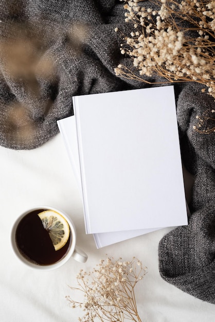 Livres vierges blancs avec une tasse de thé au citron à carreaux gris et une conception de maquette de fleurs sèches