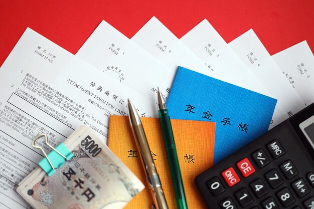 Photo des livrets d'assurance-pension japonais sur la table avec des billets en yen, un stylo et une calculatrice sur la table.