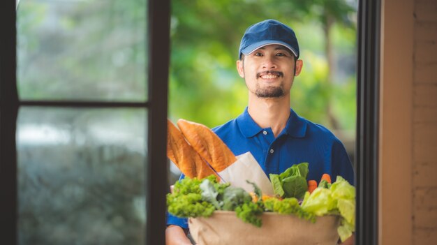 Le livreur asiatique donne le sac de l'épicerie à la femme devant sa maison