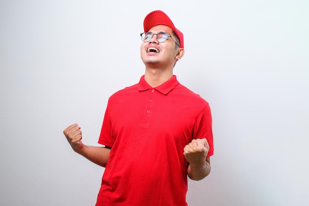 Livreur asiatique portant une casquette debout sur fond rouge isolé très heureux et excité faisant le geste du gagnant avec les bras levés souriant et criant pour le succès Concept de célébration