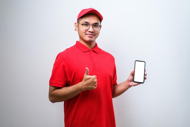 Livreur asiatique portant une casquette tenant un smartphone sur fond blanc très heureux pointant avec la main et le doigt sur le côté