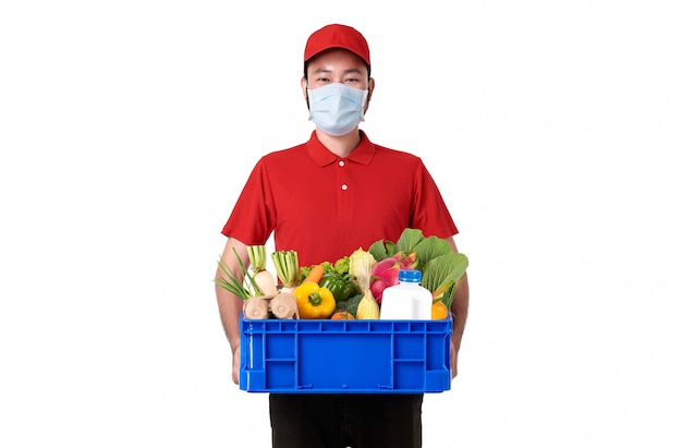 Livreur asiatique portant un masque facial en uniforme rouge tenant un panier de nourriture fraîche isolé sur fond blanc. service de livraison express pendant covid19.