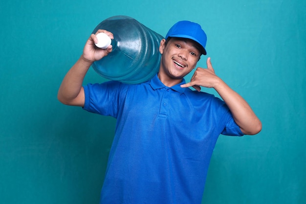 Un livreur asiatique en uniforme bleu travaille comme courrier de concessionnaire, tenant une bouteille d'eau tout en faisant du téléphone ge