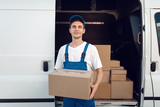 Livreur avec boîte en carton à la voiture, service de livraison. Homme en uniforme tenant un paquet de carton, homme livrer, travail de messagerie