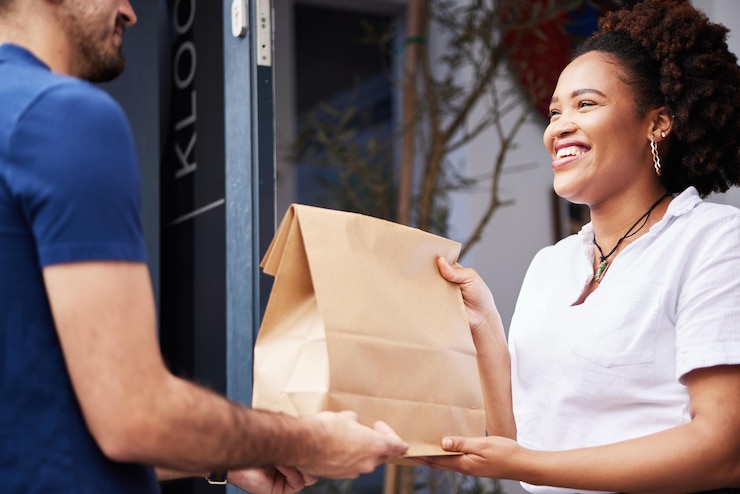 Photo livreur colis et une femme à la porte avec un sourire et un sac en papier pour le commerce électronique et l'expédition logistique achats en ligne et fret ou coursier donnant à un client satisfait une commande de restauration rapide