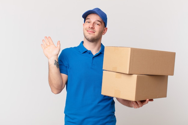 Livreur de colis homme souriant joyeusement et joyeusement, agitant la main, vous accueillant et vous saluant, ou vous disant au revoir