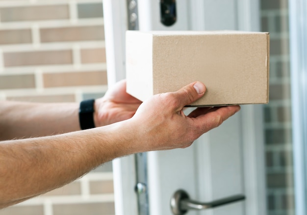 Le livreur donne la boîte en carton au client à la porte de sa maison