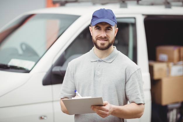 Livreur écrit sur le presse-papiers devant sa camionnette