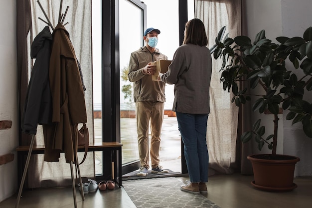 Un livreur masqué avec une boîte et un client à la maison.