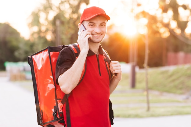 Un livreur de nourriture avec un sac à dos rouge livre des commandes par courrier masculin avec une boîte isotherme pour aliments