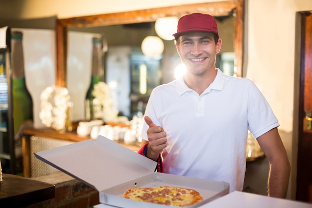 Livreur de pizza montrant une pizza fraîche et les pouces vers le haut