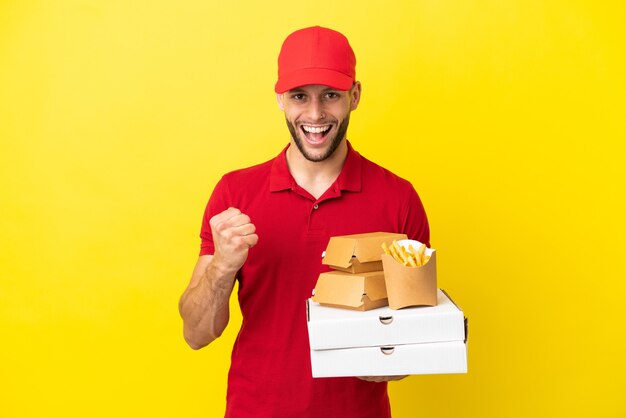 Livreur de pizza ramasser des boîtes de pizza et des hamburgers sur fond isolé célébrant une victoire en position de vainqueur