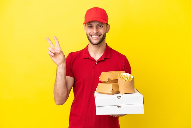 livreur de pizza ramasser des boîtes de pizza et des hamburgers sur fond isolé souriant et montrant le signe de la victoire