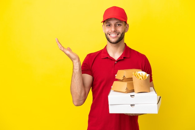 Livreur de pizza ramasser des boîtes de pizza et des hamburgers sur fond isolé tendant les mains sur le côté pour inviter à venir