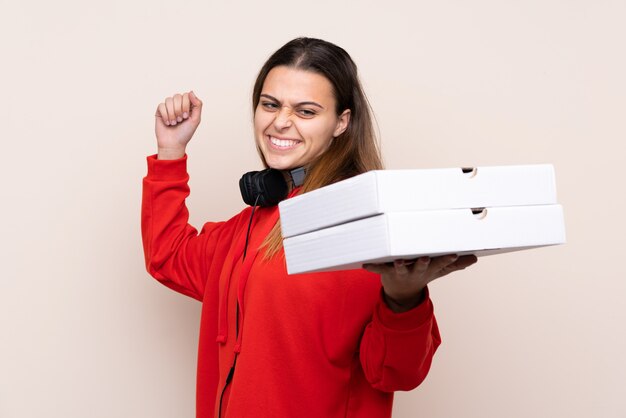 Livreur de pizza tenant une pizza sur un mur isolé célébrant une victoire