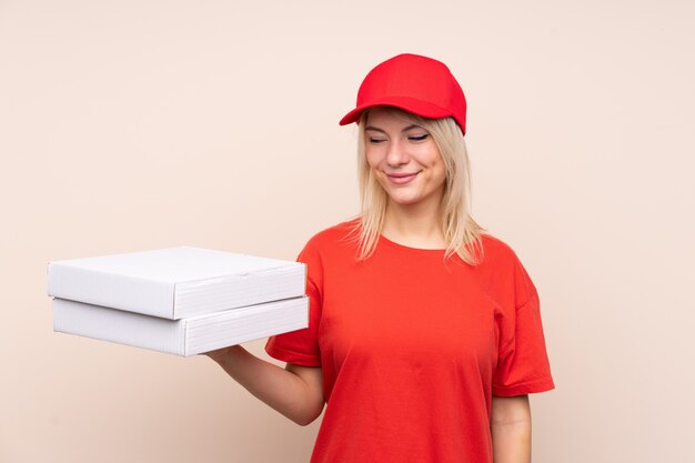 Livreur de pizza tenant une pizza sur un mur isolé avec une expression heureuse