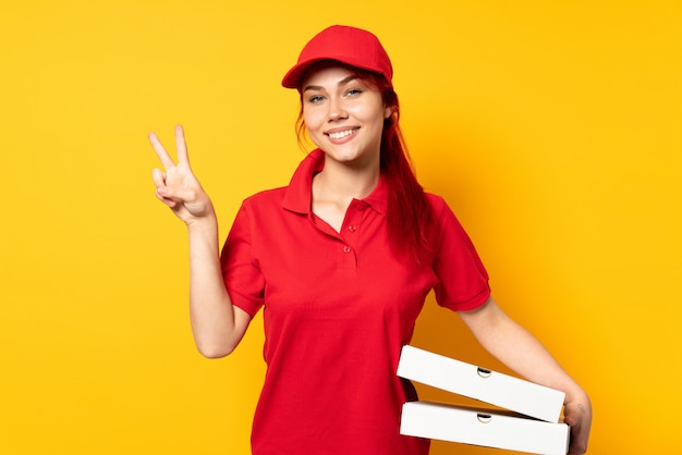 Livreur de pizza tenant une pizza sur un mur isolé montrant le signe de la victoire avec les deux mains