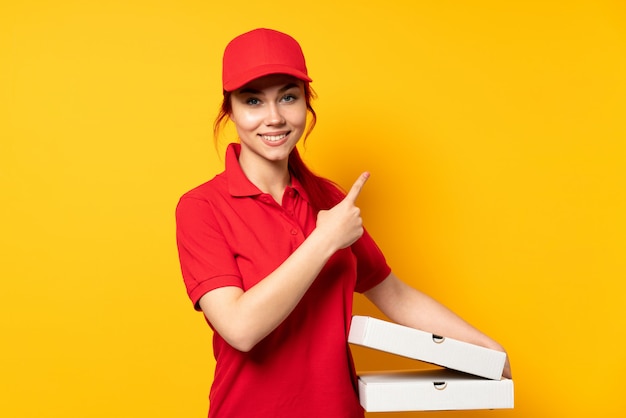 Livreur de pizza tenant une pizza sur un mur isolé pointant vers le côté pour présenter un produit