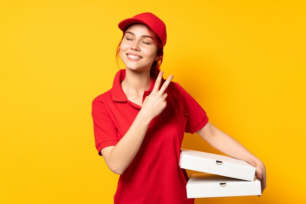 Livreur de pizza tenant une pizza sur un mur isolé, souriant et montrant le signe de la victoire