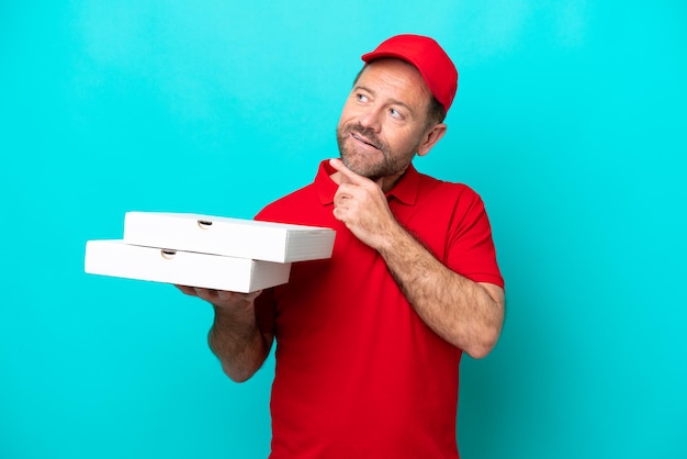 Livreur de pizza avec uniforme de travail ramassant des boîtes à pizza isolées sur fond bleu levant les yeux en souriant