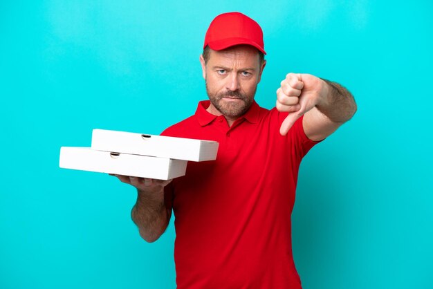 Livreur de pizza avec uniforme de travail ramassant des boîtes de pizza isolées sur fond bleu montrant le pouce vers le bas avec une expression négative