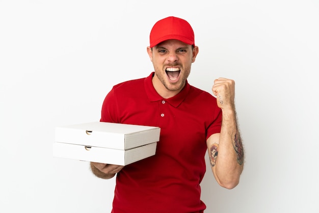 Livreur de pizza avec uniforme de travail ramassant des boîtes de pizza sur un mur blanc isolé célébrant une victoire en position de vainqueur