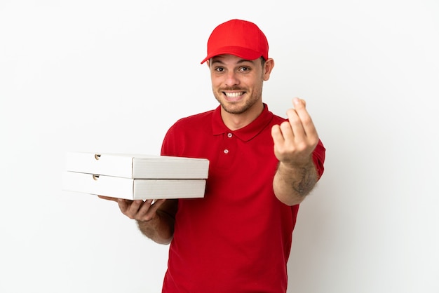 Livreur de pizza avec un uniforme de travail ramassant des boîtes de pizza sur un mur blanc isolé faisant un geste d'argent