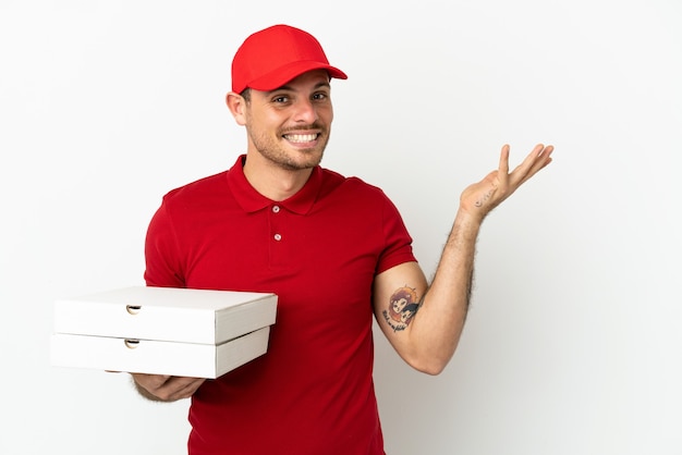 Livreur de pizza avec uniforme de travail ramassant des boîtes de pizza sur un mur blanc isolé tendant les mains sur le côté pour inviter à venir