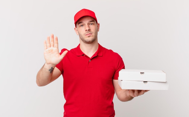 livreur de pizzas à l'air sérieux, sévère, mécontent et en colère montrant la paume ouverte faisant un geste d'arrêt