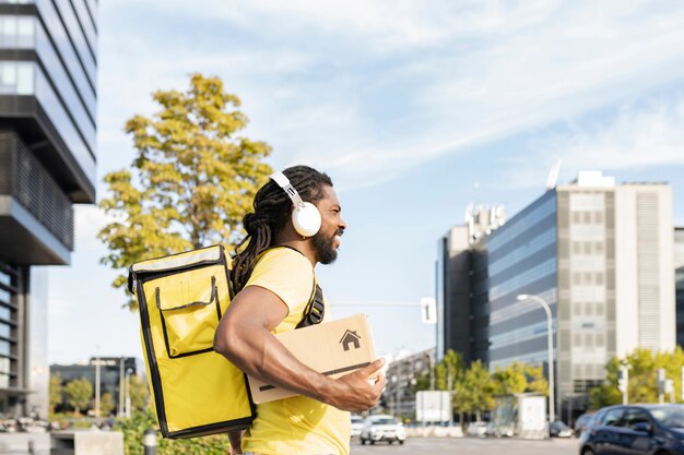 Livreur avec sac à dos et une boîte à la main, écoutant de la musique en ville