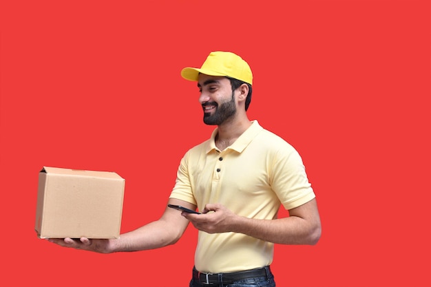 livreur en t-shirt jaune utilisant un téléphone portable et tenant une boîte d'emballage modèle pakistanais indien