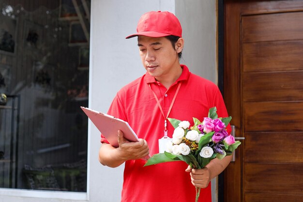 Le livreur tenant un bouquet de fleurs et vérifiant la liste de livraison sur le bloc-notes à l'extérieur