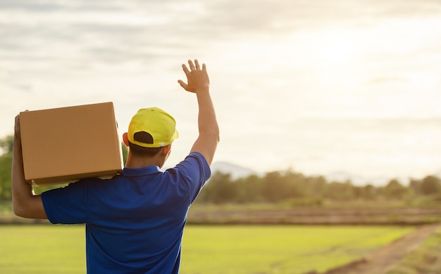 Livreur tenant un colis brun ou des boîtes en carton, livraison au client à la campagne