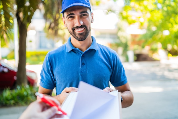 Photo livreur transportant le paquet tandis que le client signe dans le presse-papiers.