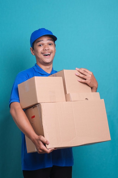 Un livreur en uniforme bleu travaille comme courrier du concessionnaire tenant une pile de boîtes en carton vierges