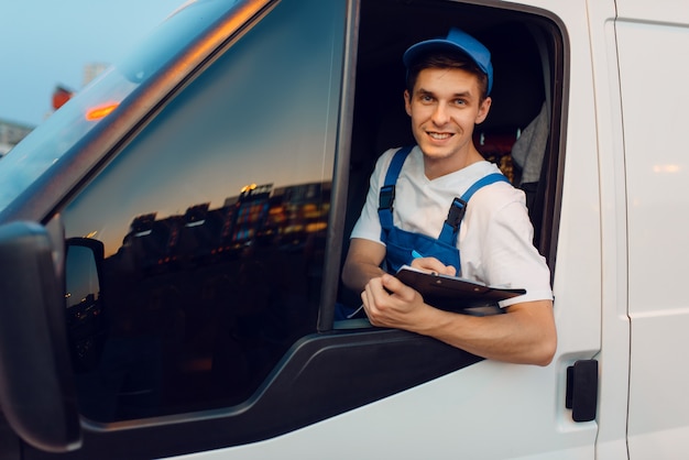 Livreur en uniforme conduit une voiture, service de livraison, livraison. Homme dans un véhicule de poste, un homme livrant, un courrier ou un travail d'expédition