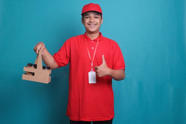 Livreur en uniforme rouge tenant une tasse à emporter dans la main et donnant le pouce vers le haut en bleu studio ba