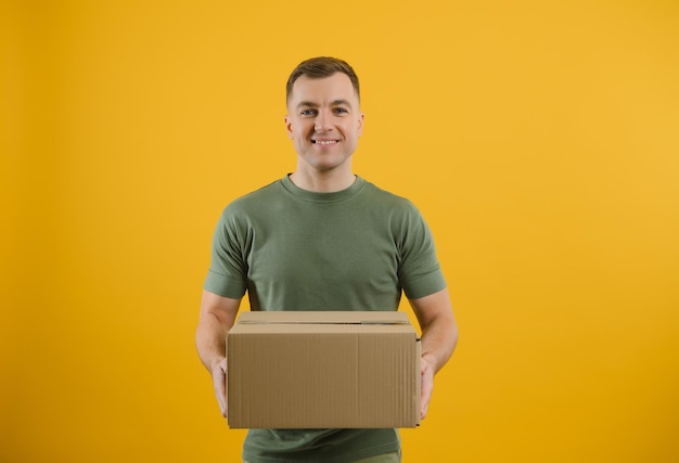 Livreur en uniforme vert isolé sur fond jaune portrait en studio Employé masculin travaillant comme concessionnaire de messagerie tenir une boîte en carton vide Concept de service Maquette espace de copie