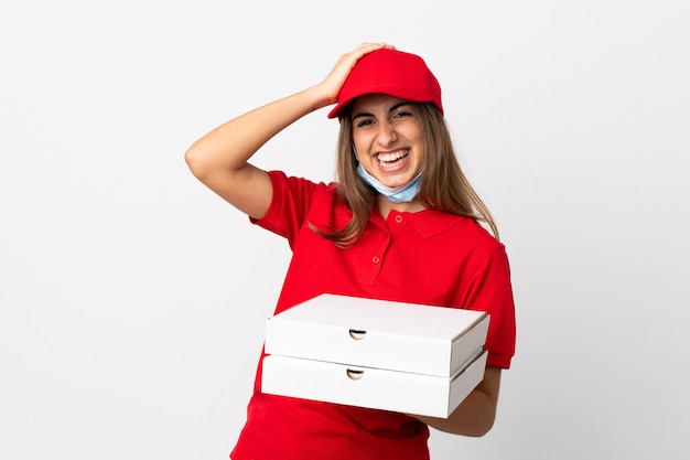 Une livreuse de pizza tenant une pizza et se protégeant du coronavirus avec un masque sur un mur blanc isolé a réalisé quelque chose et a l'intention de trouver la solution