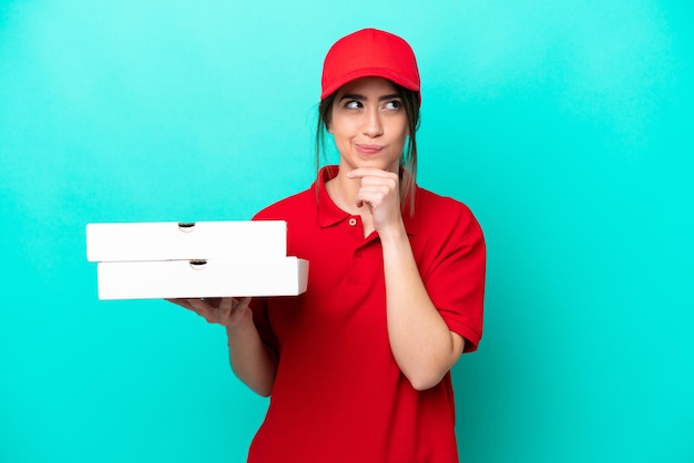 Livreuse de pizza avec uniforme de travail ramassant des boîtes de pizza isolées sur fond bleu ayant des doutes et pensant