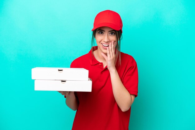 Livreuse de pizza avec uniforme de travail ramassant des boîtes de pizza isolées sur fond bleu avec une expression faciale surprise et choquée
