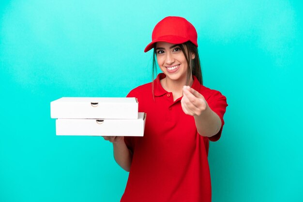 Livreuse de pizza avec uniforme de travail ramassant des boîtes de pizza isolées sur fond bleu faisant un geste d'argent