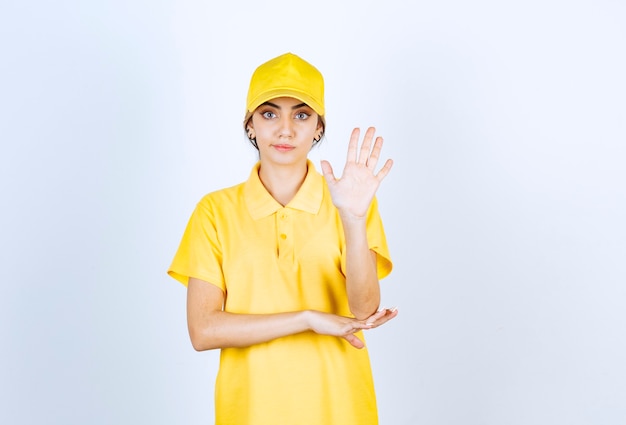 Livreuse en uniforme jaune debout et montrant la paume ouverte.