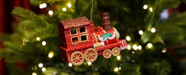 Locomotive jouet en verre brillant rouge accroché à l'arbre de Noël avec guirlande