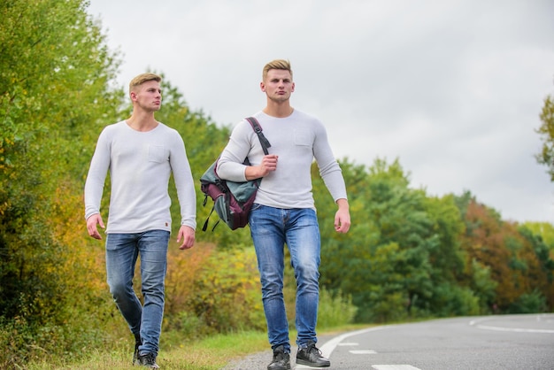 Éloignez-vous de voyager en faisant de l'auto-stop road trip wanderlust concept Randonnée avec des amis cool partis pour se retrouver Voyage et auto-stop jumeaux marchant le long de la route faisant de l'auto-stop sur une route vide