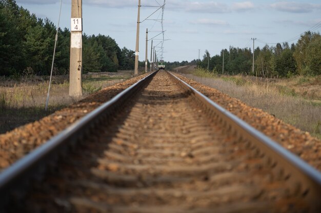 Loin à l'horizon, la locomotive du train se dirige vers la caméra le long des rails du chemin de fer par une claire journée d'été