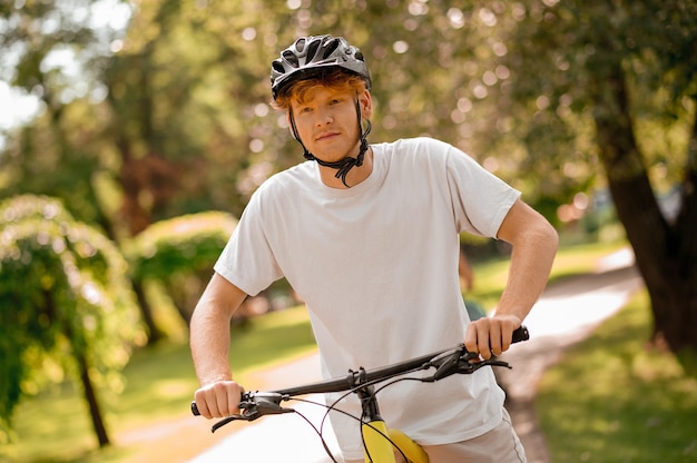 Loisirs actifs. Mec pacifique optimiste en tshirt blanc en casque à vélo passant du temps dans un parc verdoyant par beau temps