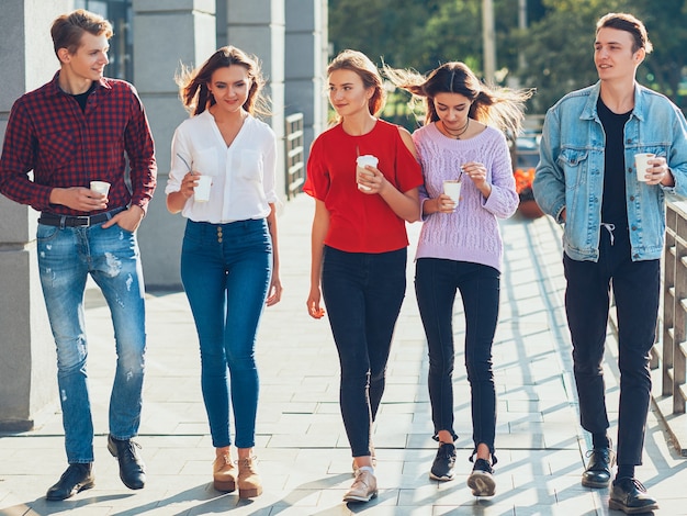 Loisirs ados. Amusement de communication sociale. Groupe d'amis féminins masculins marchant avec du café à emporter.