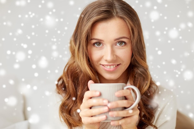 loisirs, boissons, hiver et concept de personnes - gros plan d'une jeune femme heureuse avec une tasse de café ou de thé à la maison sur la neige